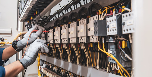 Eine Person in einem blauen Hemd und Handschuhen arbeitet an elektrischen Geräten.